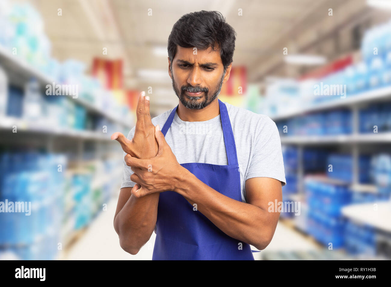 Sb-Warenhaus oder Supermarkt indischen männlichen Mitarbeiter berühren Handgelenk verstaucht wie körperliche Anstrengung schmerzen Konzept Stockfoto