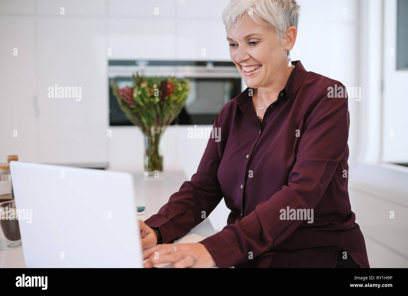Porträt einer wunderschöne reife Frau lächelnd, die Eingabe auf Ihrem Laptop, in der Küche Stockfoto