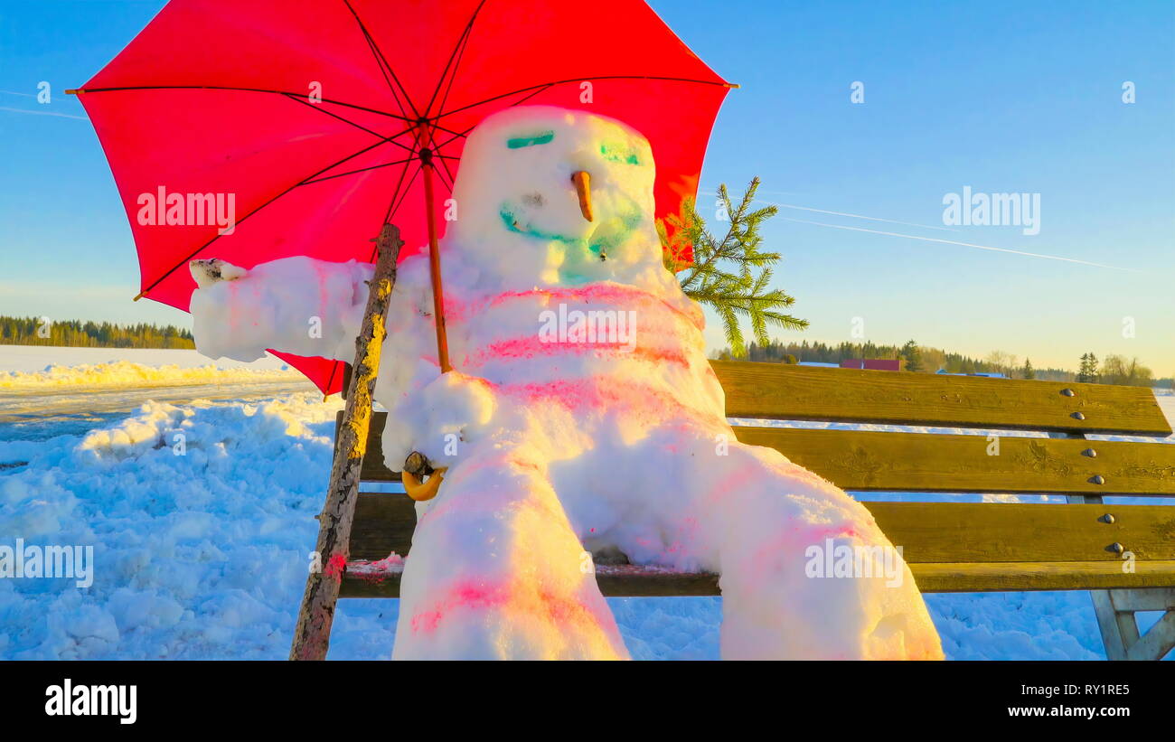 Ein sitzender Schneemann auf der Bank, er hat eine Karotte Nase ein Stick auf seiner Hand und einen Schirm auf dem Rücken Stockfoto