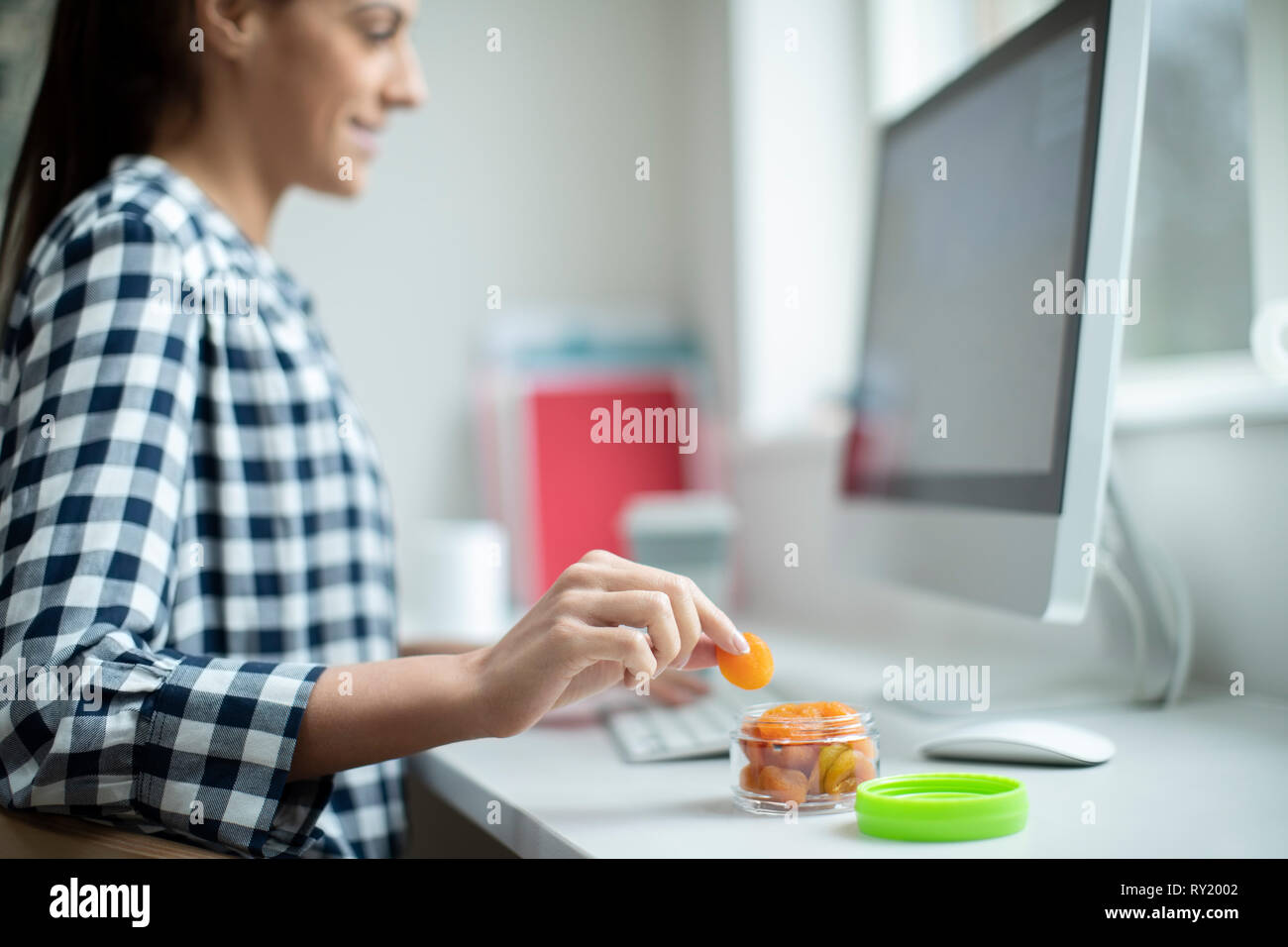 Mitarbeiterin im Büro in gesunden Snack von getrockneten Aprikosen am Schreibtisch Stockfoto