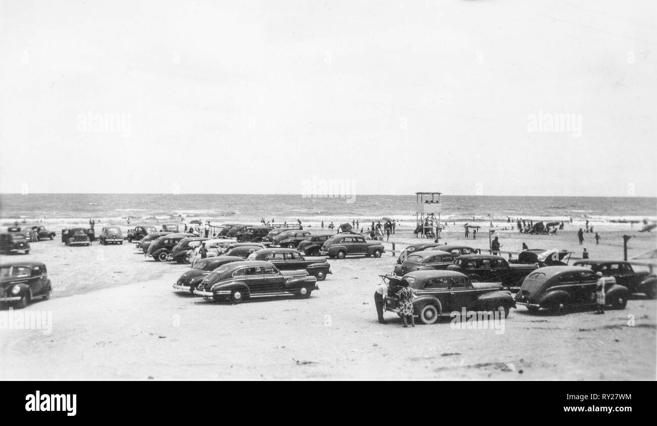 Horizontale schwarze und weiße Foto von Menschen und Autos am Strand in den späten 1940er Jahren. Stockfoto