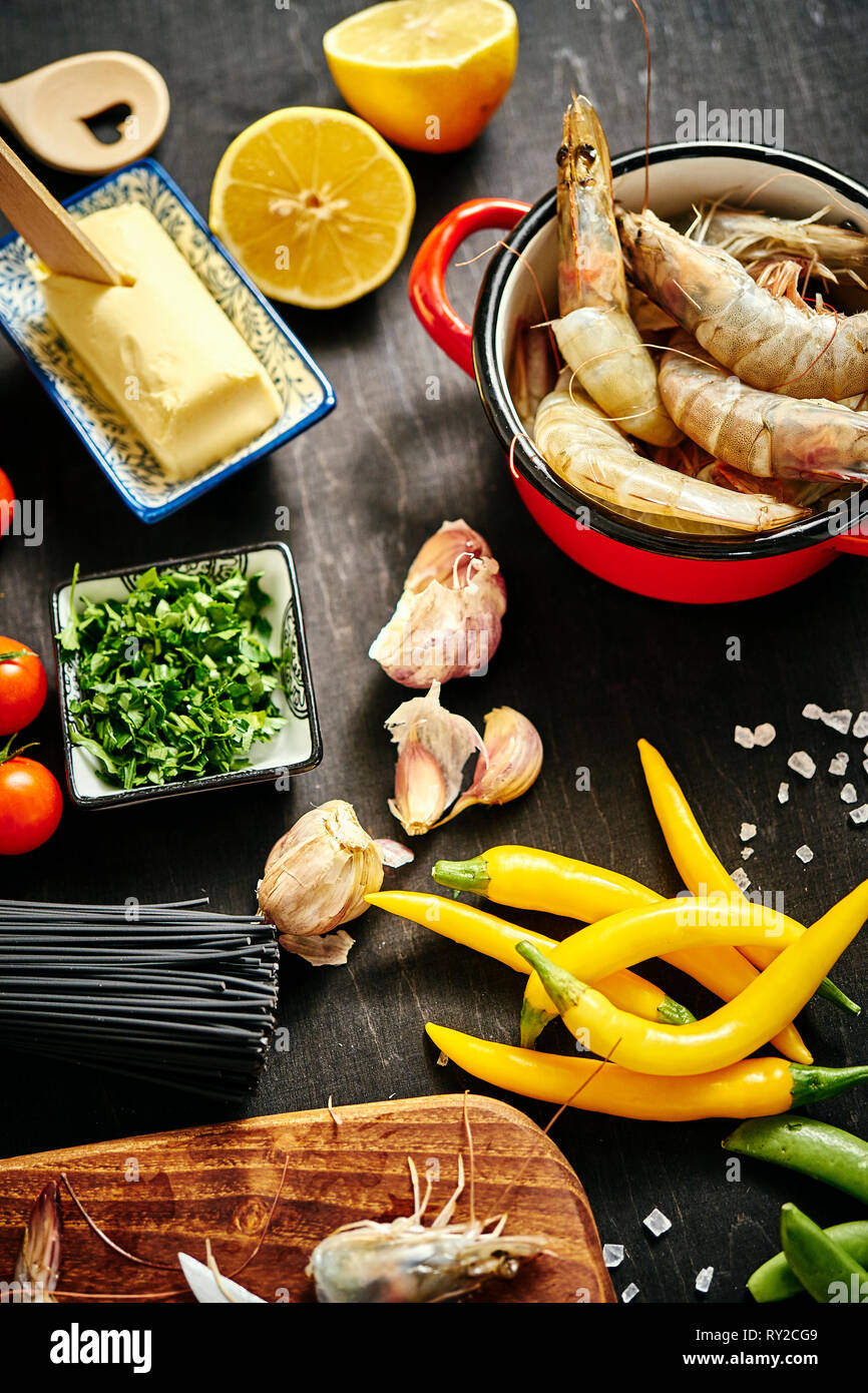 Frische und köstliche rohe Riesengarnelen in einem roten Topf mit Petersilie, Zitrone, Butter, Tomaten und Peperoni Stockfoto