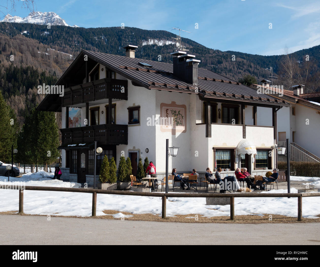 Italien Cafe - die Leute draußen sitzen ein Cafe im Schnee mit Winter Sonnenschein im März; Pinzolo Dorf, Brenta Dolomiten, nördliche Italien Europa Stockfoto