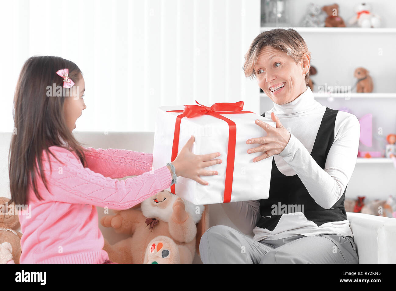 Mutter und Tochter mit Geschenkbox sitzen auf der Couch. Das Konzept der Überraschung Stockfoto