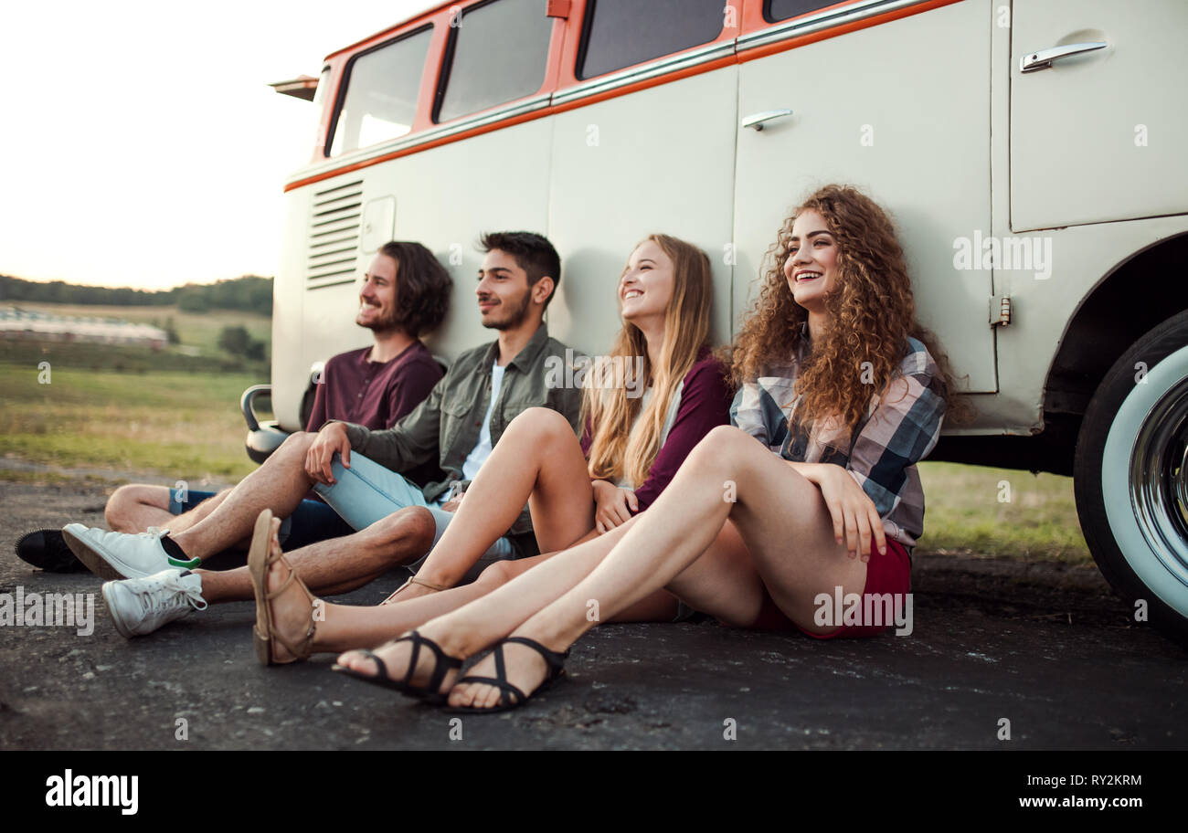 Eine Gruppe junger Freunde auf einem Roadtrip durch Landschaft, sitzend von einem minivan. Stockfoto