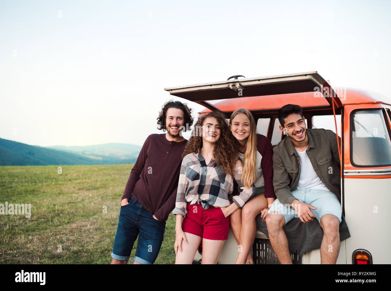 Eine Gruppe junger Freunde auf einem Roadtrip durch die Landschaft, die von einem minivan. Stockfoto