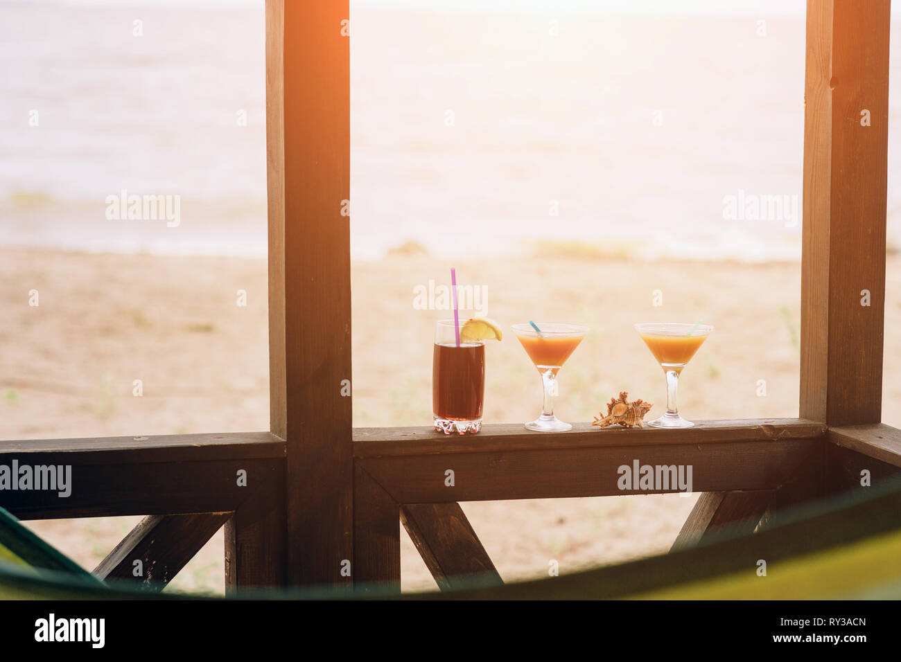 Frische exotische Cocktails auf hölzernen Rand. Shell liegt zwischen Brille. Cola mit Strohhalm und Zitrone. Flanke von Haus. Blick auf das Meer. Stockfoto