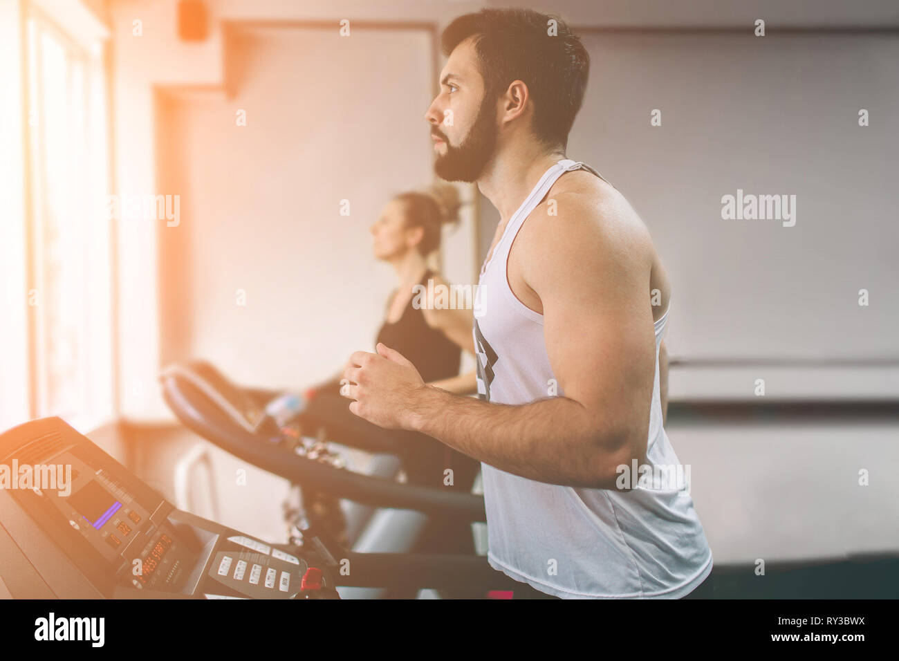 Junge Mann in Sportkleidung auf Laufband im Fitnessstudio. Muskulöse bärtigen Sportler während des Trainings. Nahaufnahme von jungen athletischen weiblichen Modell Züge bei Stockfoto