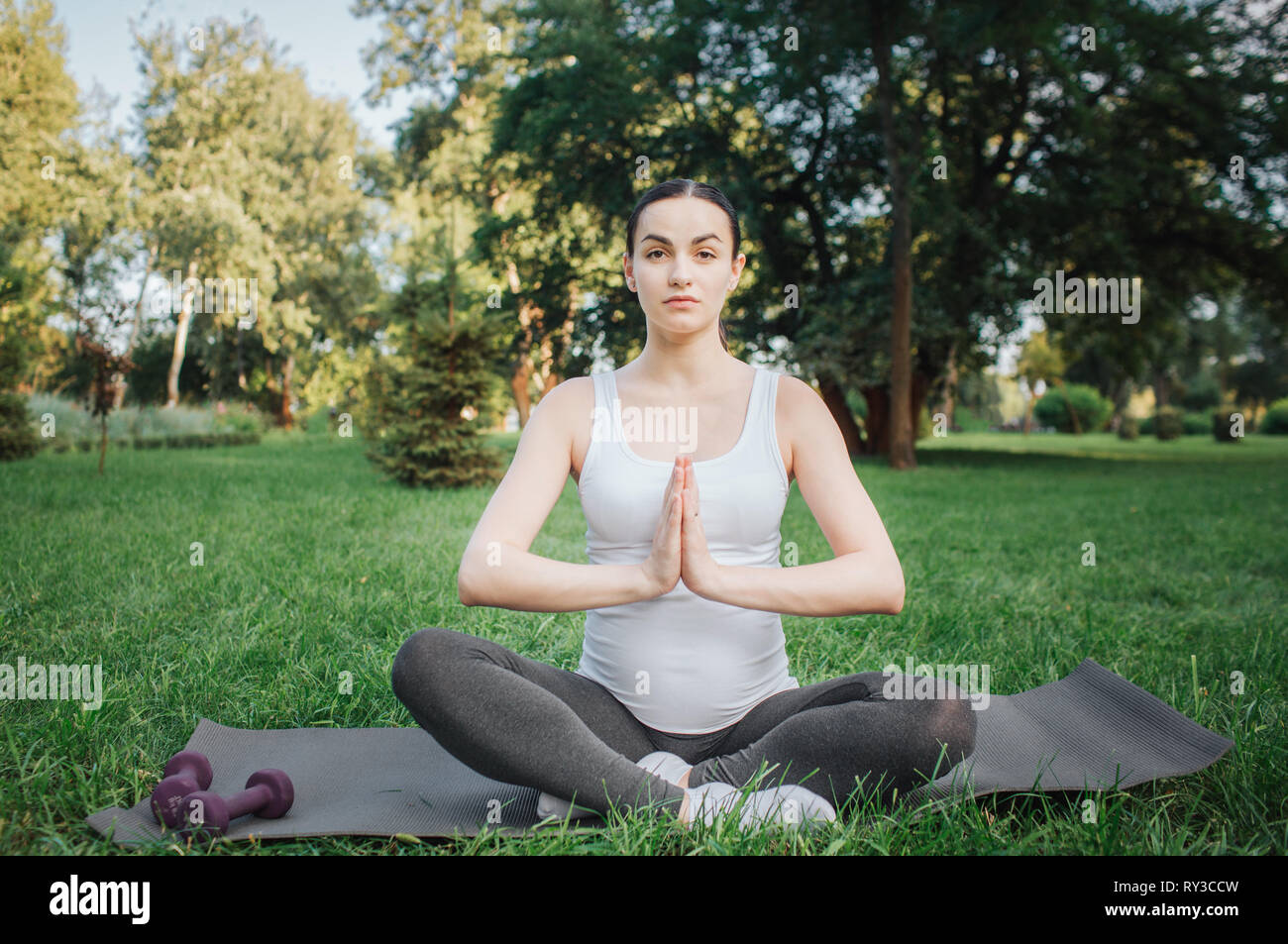 Junge schwangere Frau meditieren außerhalb. Sie sitzen auf Yoga mate im Lotussitz. Modell Hände im Gebet. Stockfoto