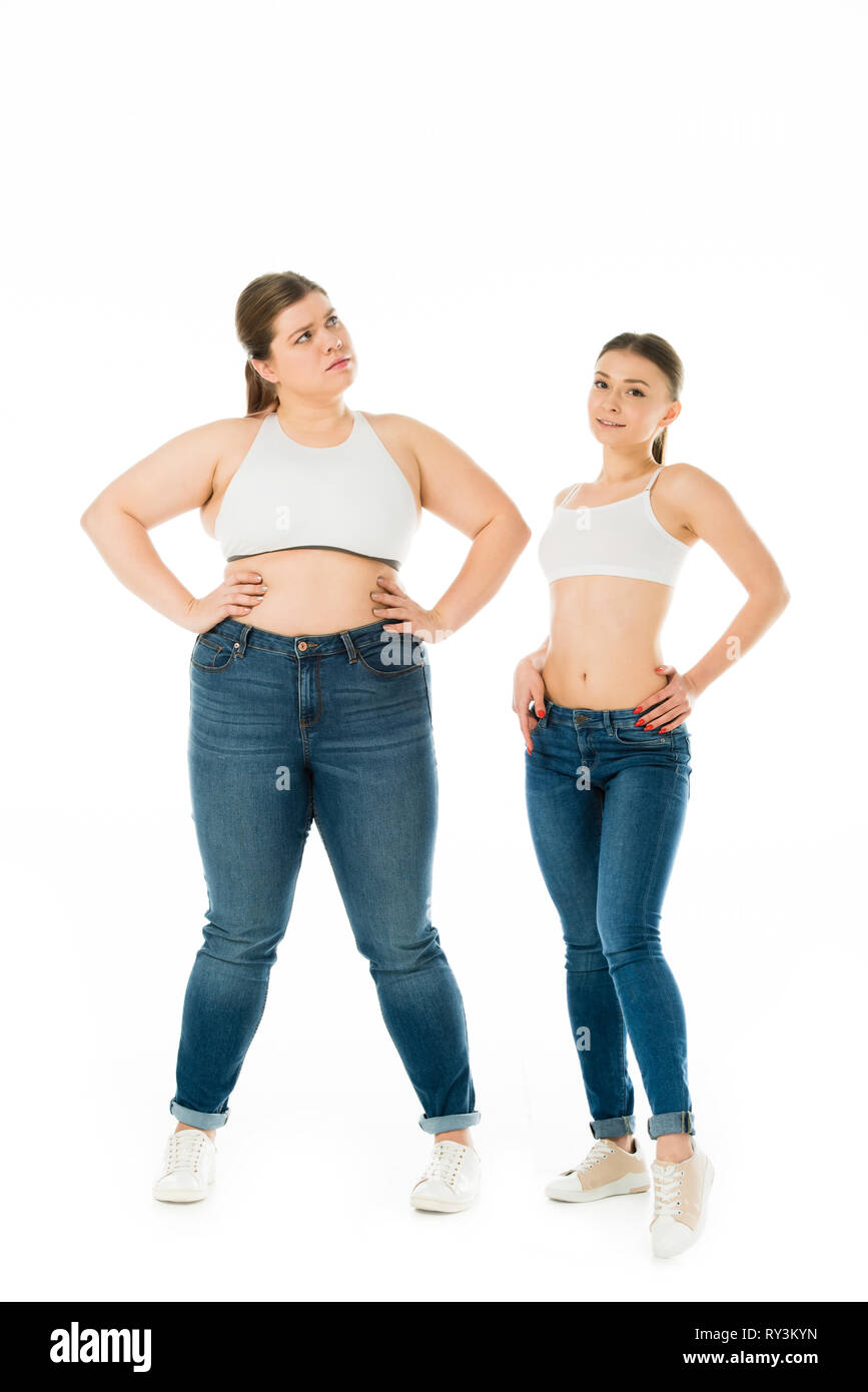 Fröhlich schlankes und traurig übergewichtige Frauen in Jeans auf den Hüften zusammen auf Weiß, Körper Positivität Konzept isoliert Posing Stockfoto