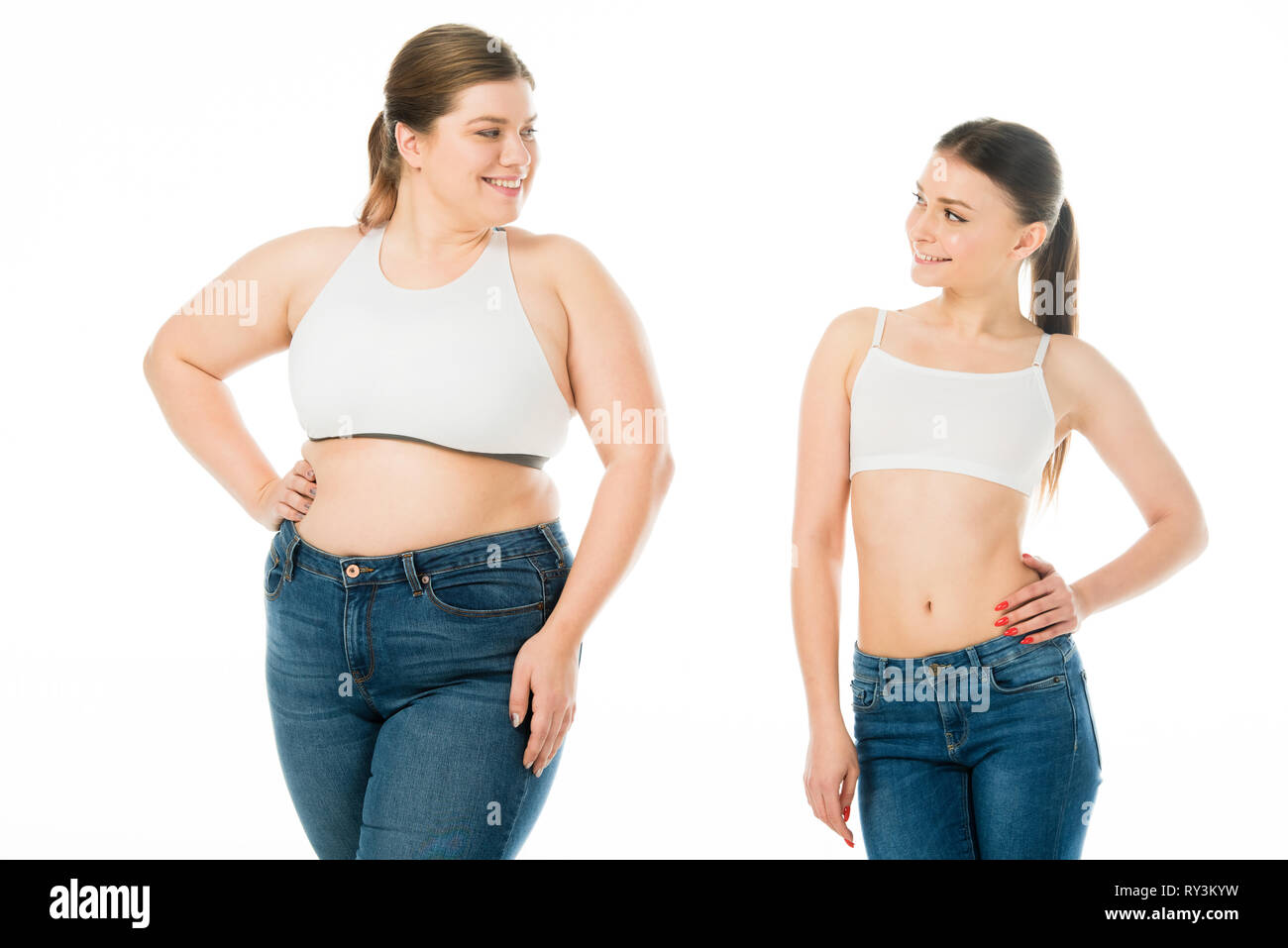 Lächelnd schlanke Frau an übergewichtigen Frau in Denim auf Weiß, Körper Positivität Konzept isoliert auf der Suche Stockfoto