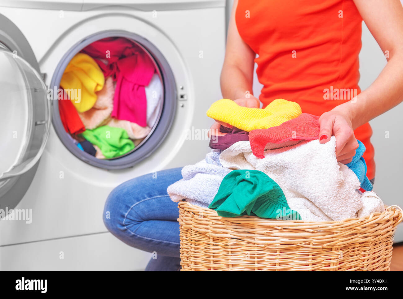 Junge Frau lädt die Wäsche in die Waschmaschine aus dem wäschekorb vor dem Waschen. Stockfoto