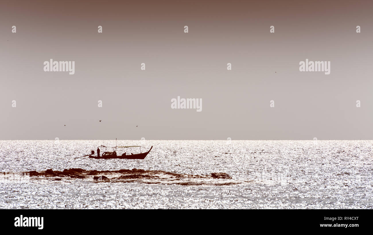 Silhouette kleines Fischerboot und einheimische Fischer auf dem Meer, schöne Landschaft der Küsten auf Koh Tarutao, Satun, Thailand in Sepia zwei ton Co Stockfoto