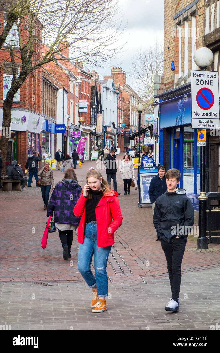 Frau Mädchen entlang eine High Street Einkaufsstraße sprechen mit ihrem Mobiltelefon in der Shropshire Markt Stadt Oswestry England Stockfoto