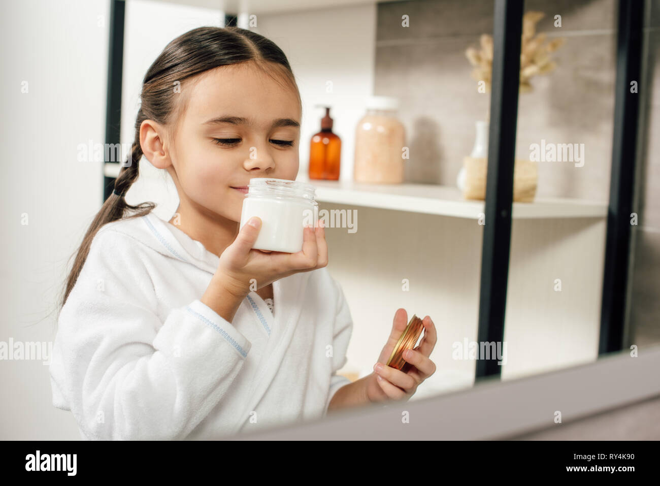 Selektiver Fokus Kind im weißen Bademantel auf der Suche nach Spiegel und Schnüffeln kosmetische Creme im Badezimmer Stockfoto