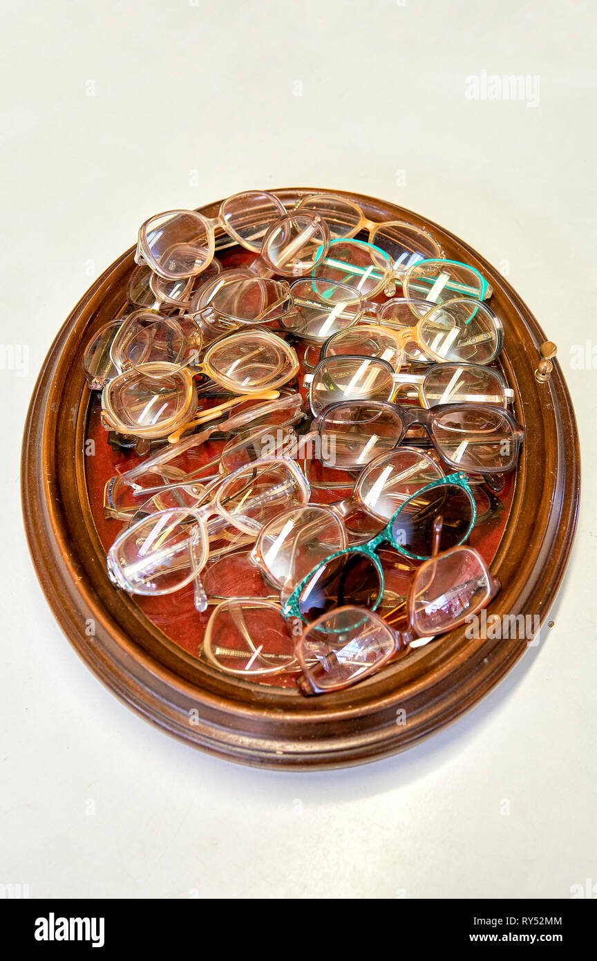 In einem Bilderrahmen liegen viele verschiedene Brillengestelle in einem Gebrauchtwarenlgeschaeft. Stockfoto