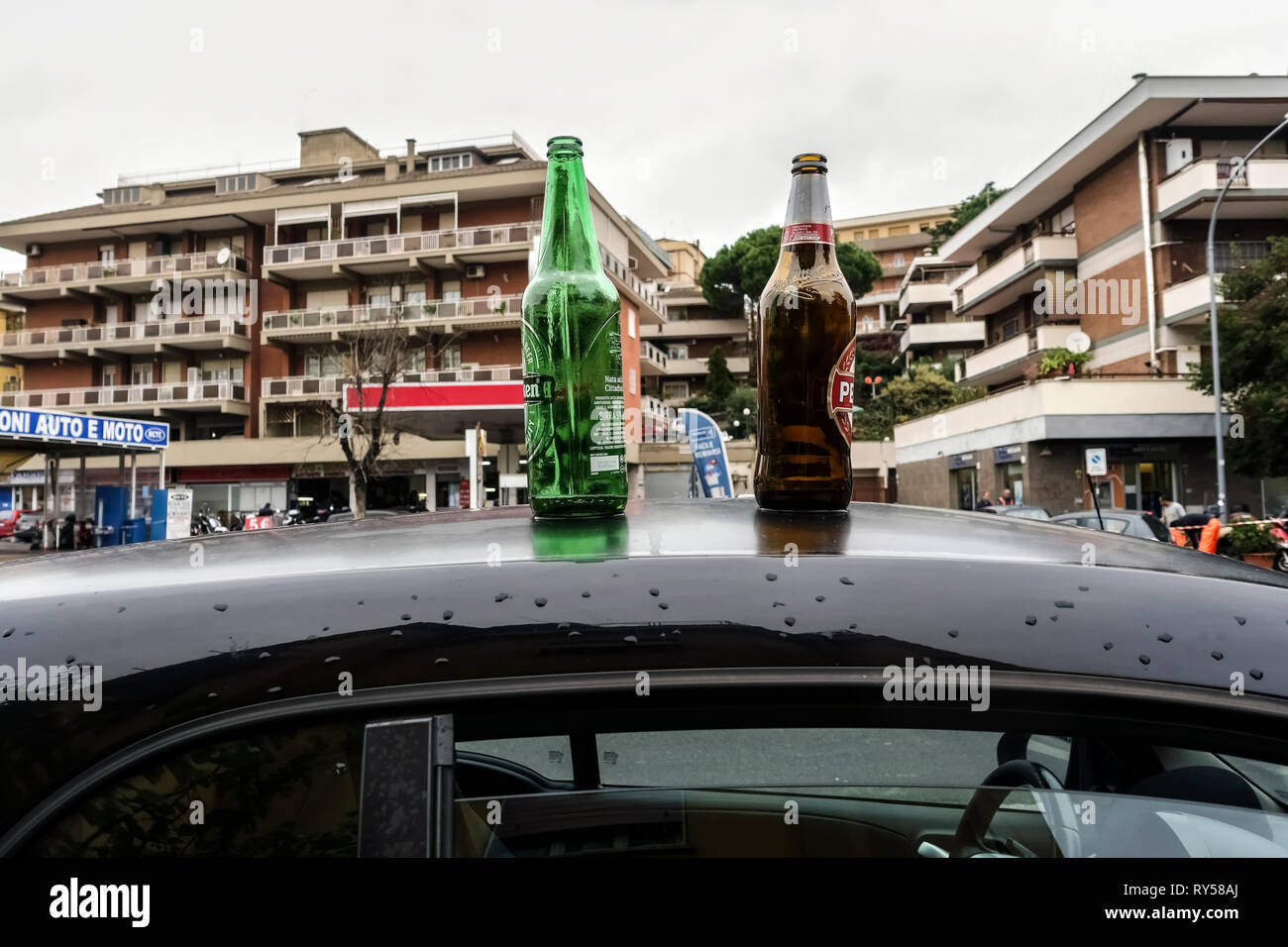 Zwei leere Bierflaschen auf einem Autodach parken auf der Straße. Konzept der Alkoholabhängigkeit. Unscharfer Hintergrund. Rom, Italien, Europa, Europäische Union, EU. Stockfoto