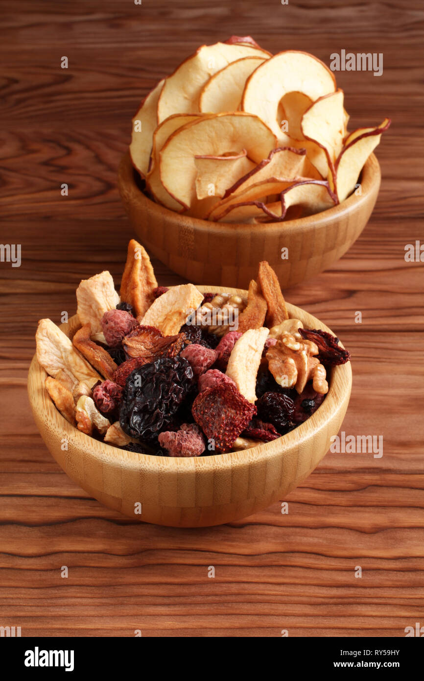 Mischung aus getrockneten Früchten Stücke von Apfel und Birne, getrocknete blaue Pflaumen, Erdbeeren, Himbeeren, Kirschen, Walnüsse in eine Schüssel, und Bambus apple Chips in einem Stockfoto