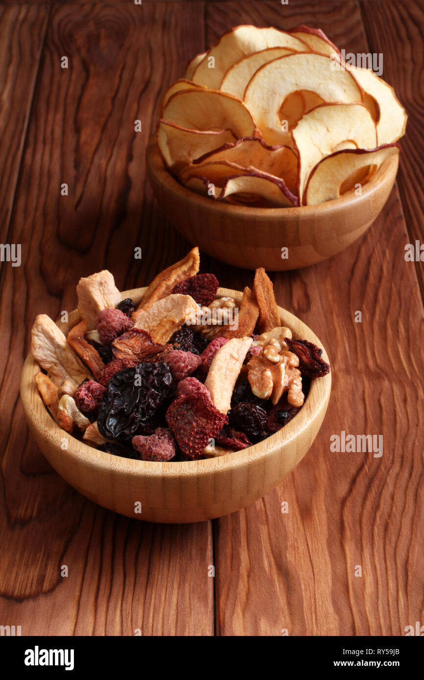 Mischung aus getrockneten Früchten Stücke von Apfel und Birne, getrocknete blaue Pflaumen, Erdbeeren, Himbeeren, Kirschen, Walnüsse in eine Schüssel, und Bambus apple Chips in einem Stockfoto