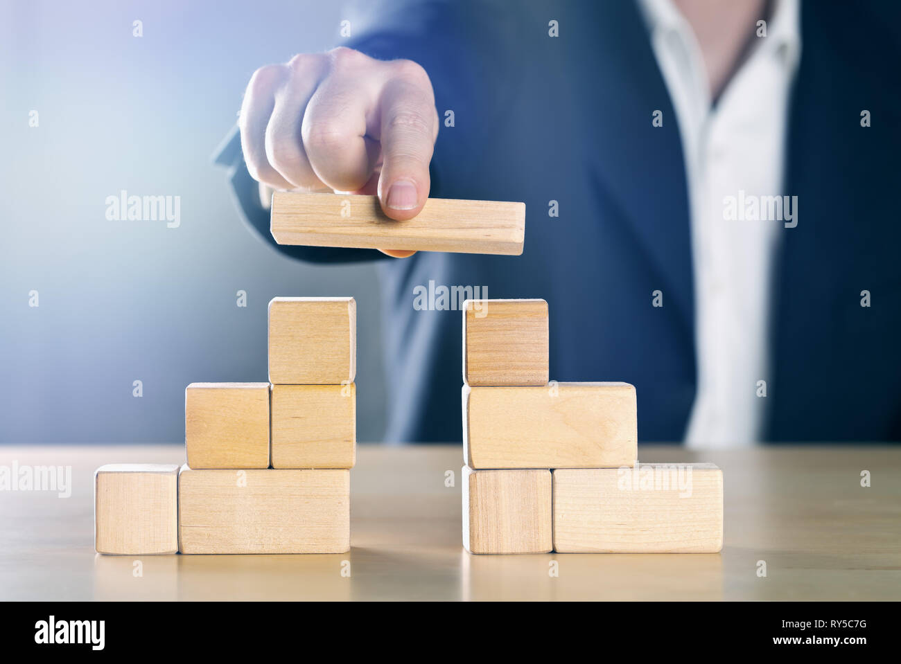 Man schließt die Lücke zwischen zwei Türme oder Parteien aus Holzklötzen; Konfliktmanagement oder Mediator Konzept, blau getönt mit ligth Fl Stockfoto