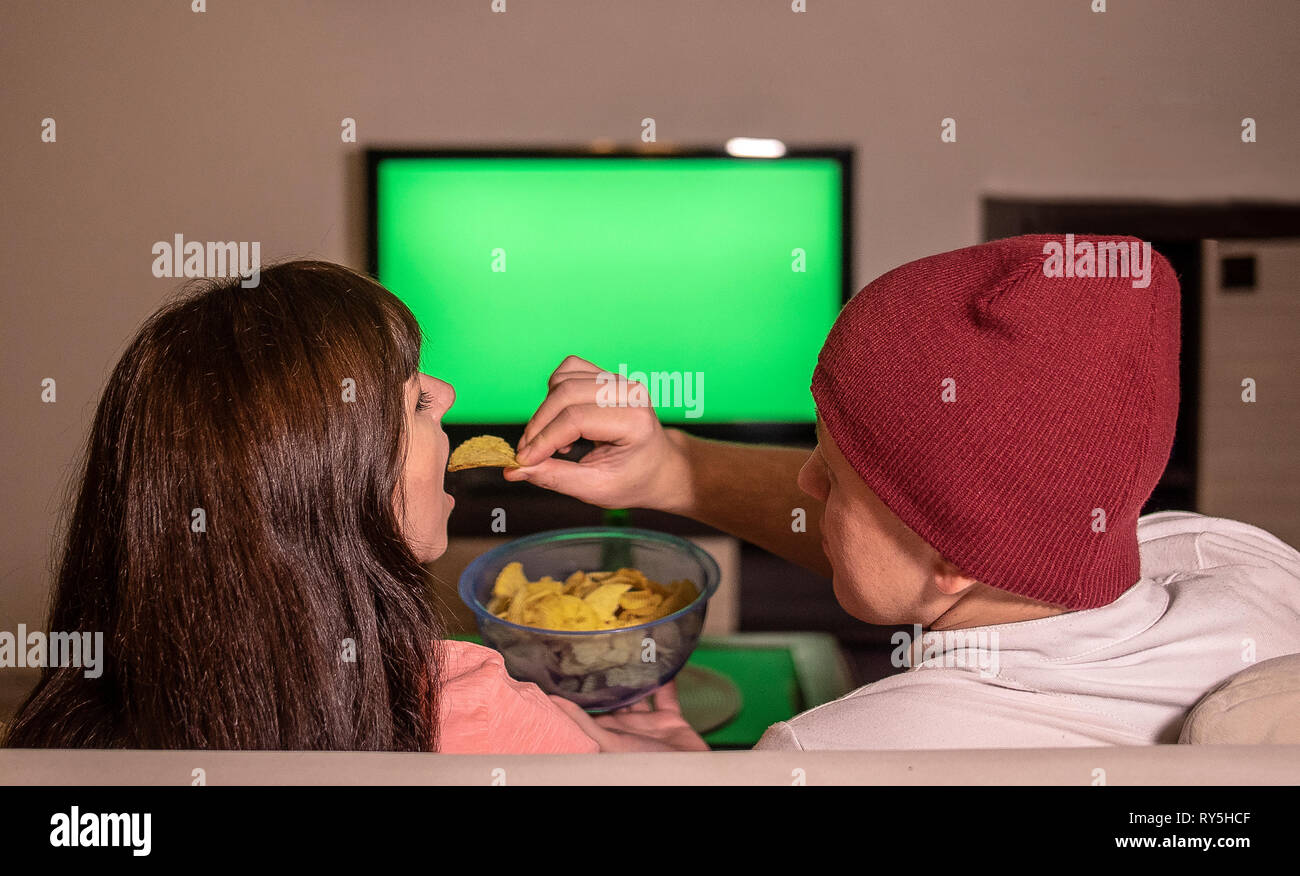 Ein Ehepaar sitzt zu Hause auf dem Sofa, am Abend vor dem Fernseher und isst Chips. Stockfoto