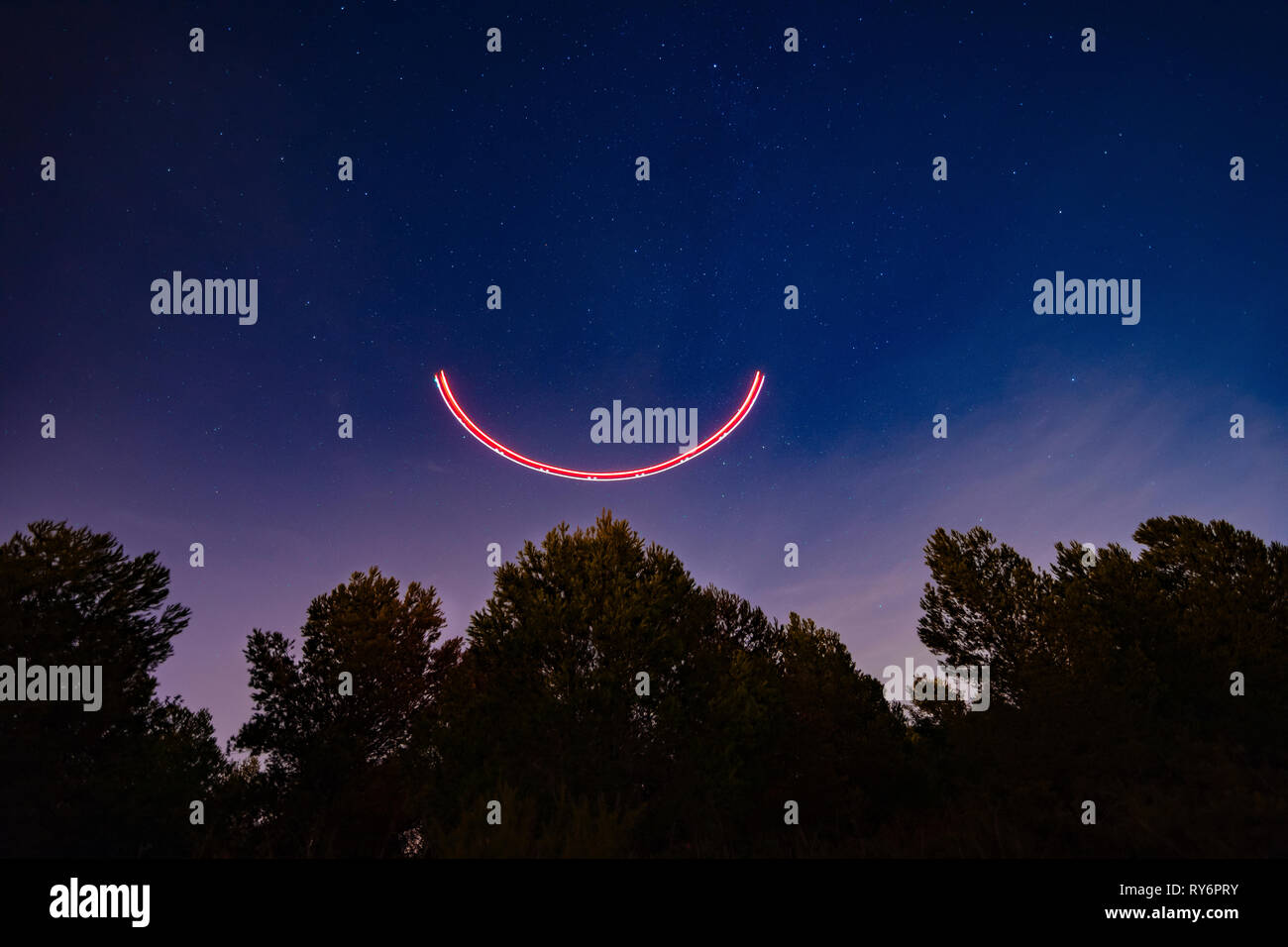 Low Angle View von Licht Malerei über Bäume gegen den blauen Himmel in der Nacht Stockfoto