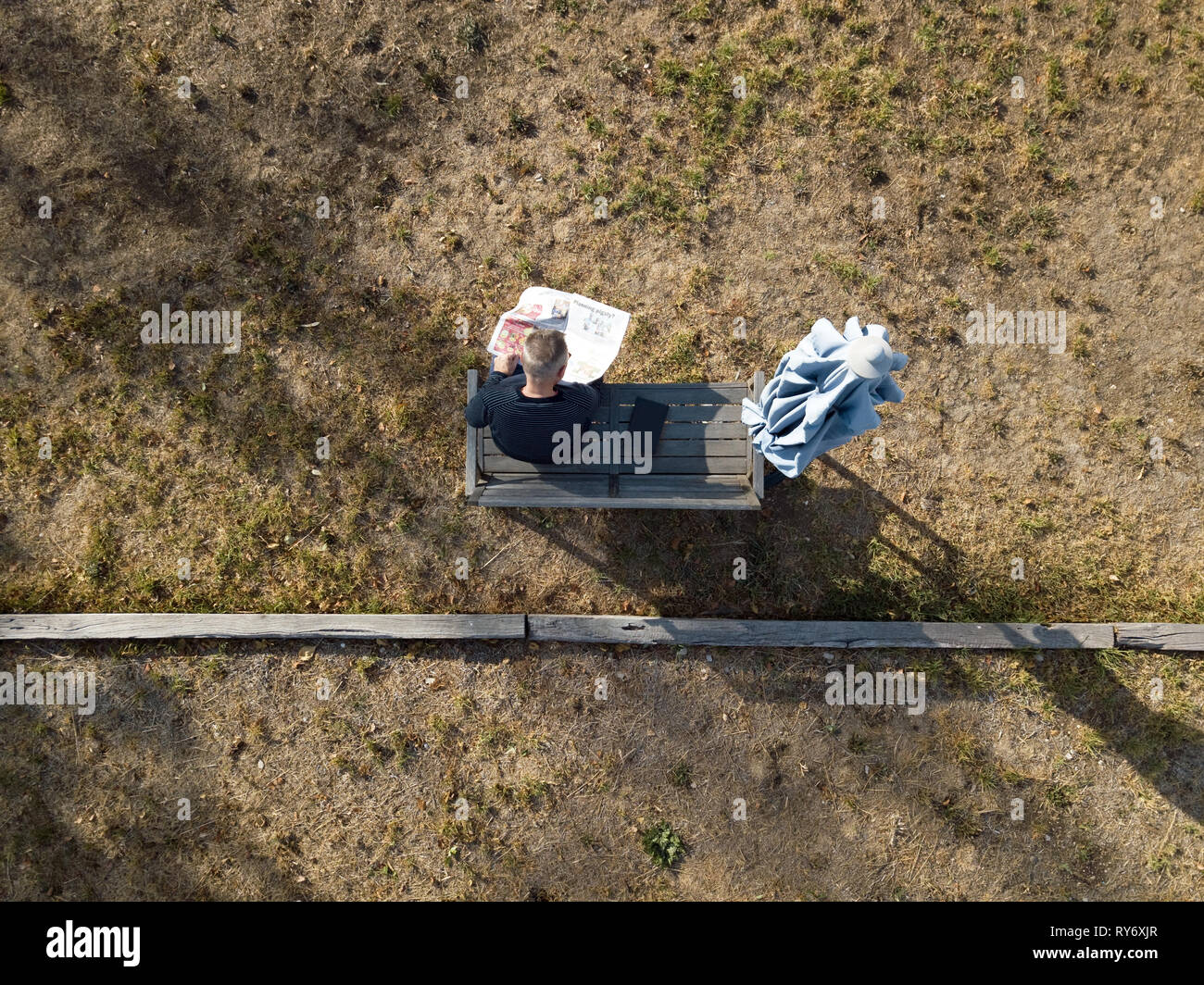 Australischen Rentner oder alten Mann lesen Zeitung außerhalb, sitzen auf den Outdoor Bank in eine Grünfläche. Luftaufnahmen in Victoria, Australien. Stockfoto