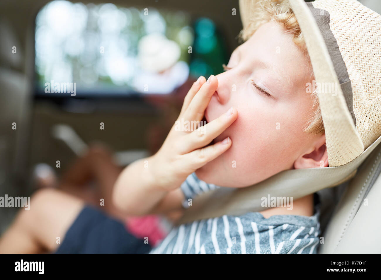 Junge hält die Hand über den Mund beim Gähnen auf der Reise im Auto in den Urlaub Stockfoto
