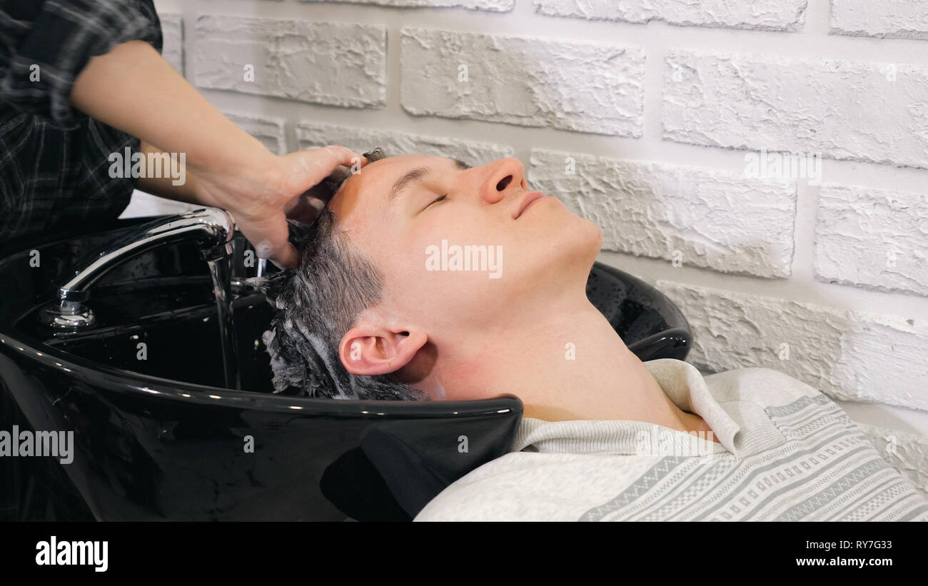 Friseur Hände waschen dunkle männliche Haar unter fließendem Wasser Im Barbershop. Stockfoto