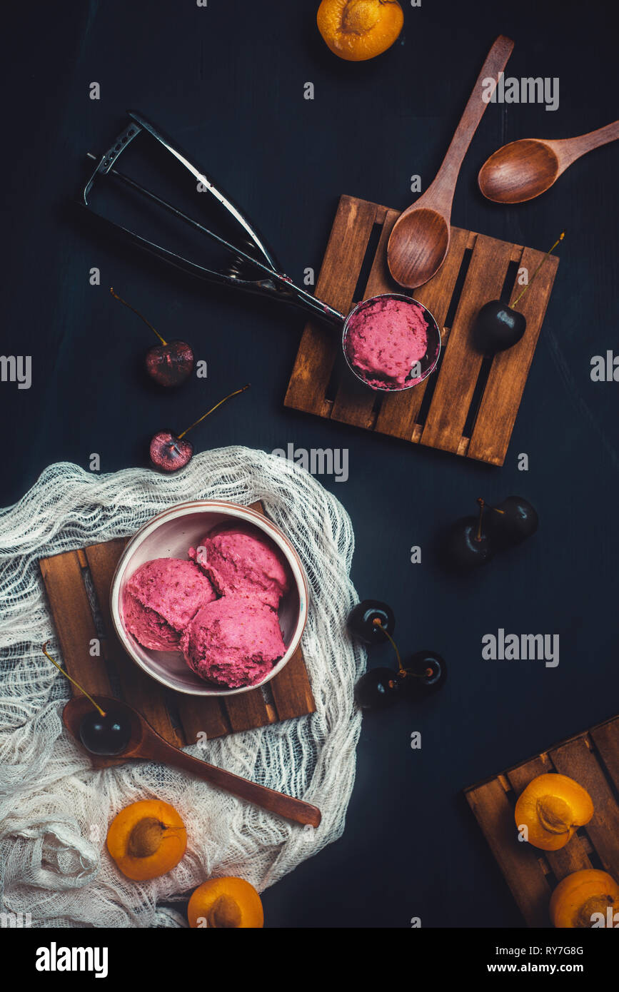 Hausgemachte rosa Eis in Eis Löffel mit Kirschen und Pflaumen. Dunkle essen Fotografie mit Kopie Raum Stockfoto