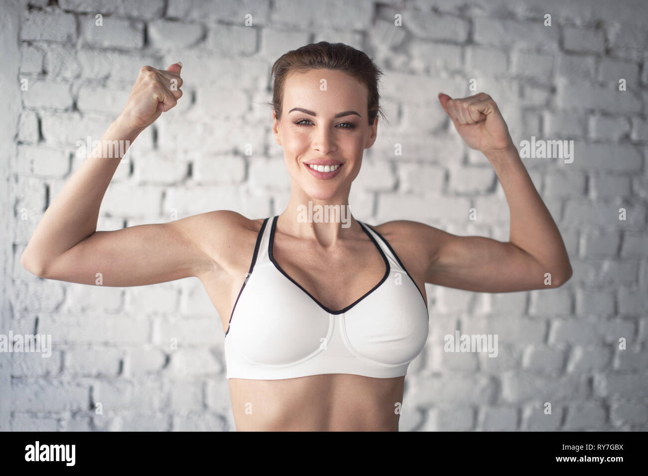 Junge starke passende Frau anzeigen bicepses Portrait in der Turnhalle Stockfoto
