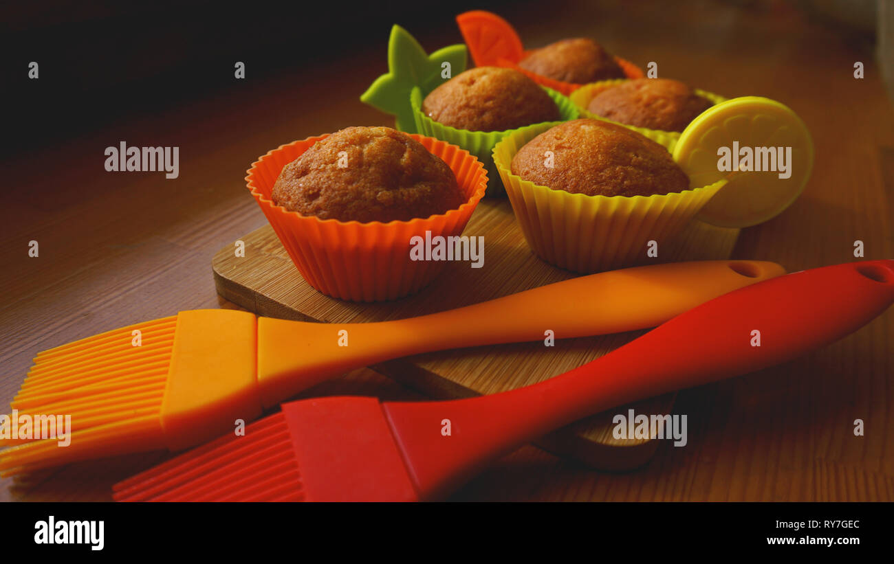 Einfachen mini Muffins in bunten Silikon Backformen. Silikon cup baking Cupcakes und Silikon Pinsel. Küche und kochen Konzept auf hölzernen Hintergrund Stockfoto