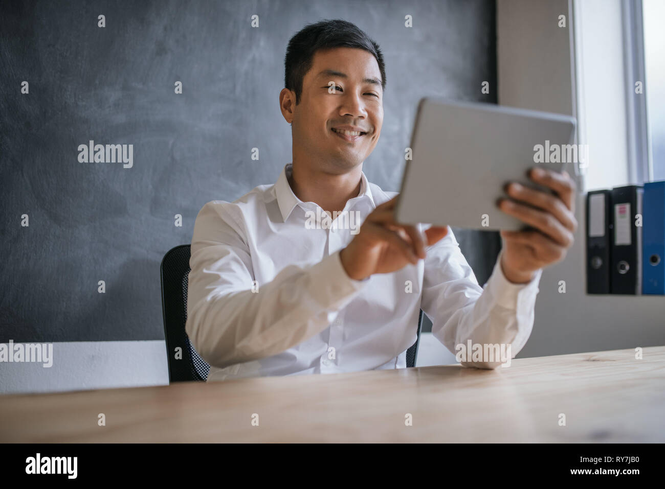 Lächelnd asiatische Geschäftsmann mit einem Tablet in seinem Büro Schreibtisch Stockfoto