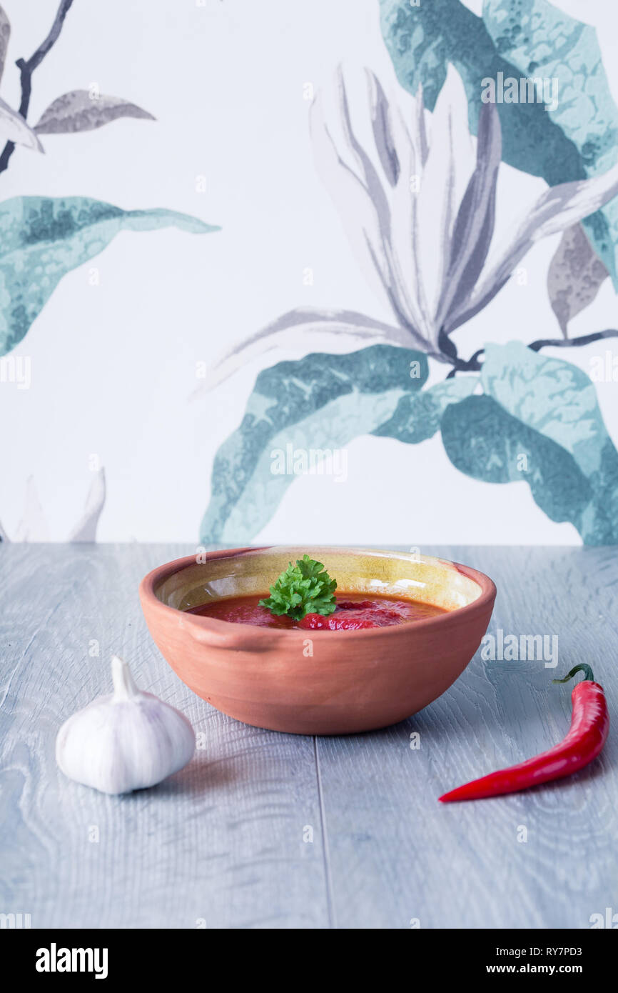 Tomatensauce in eine Schüssel geben und mit frischen Kräutern, Chili und Knoblauch vor Blumenmuster wallpaper Stockfoto
