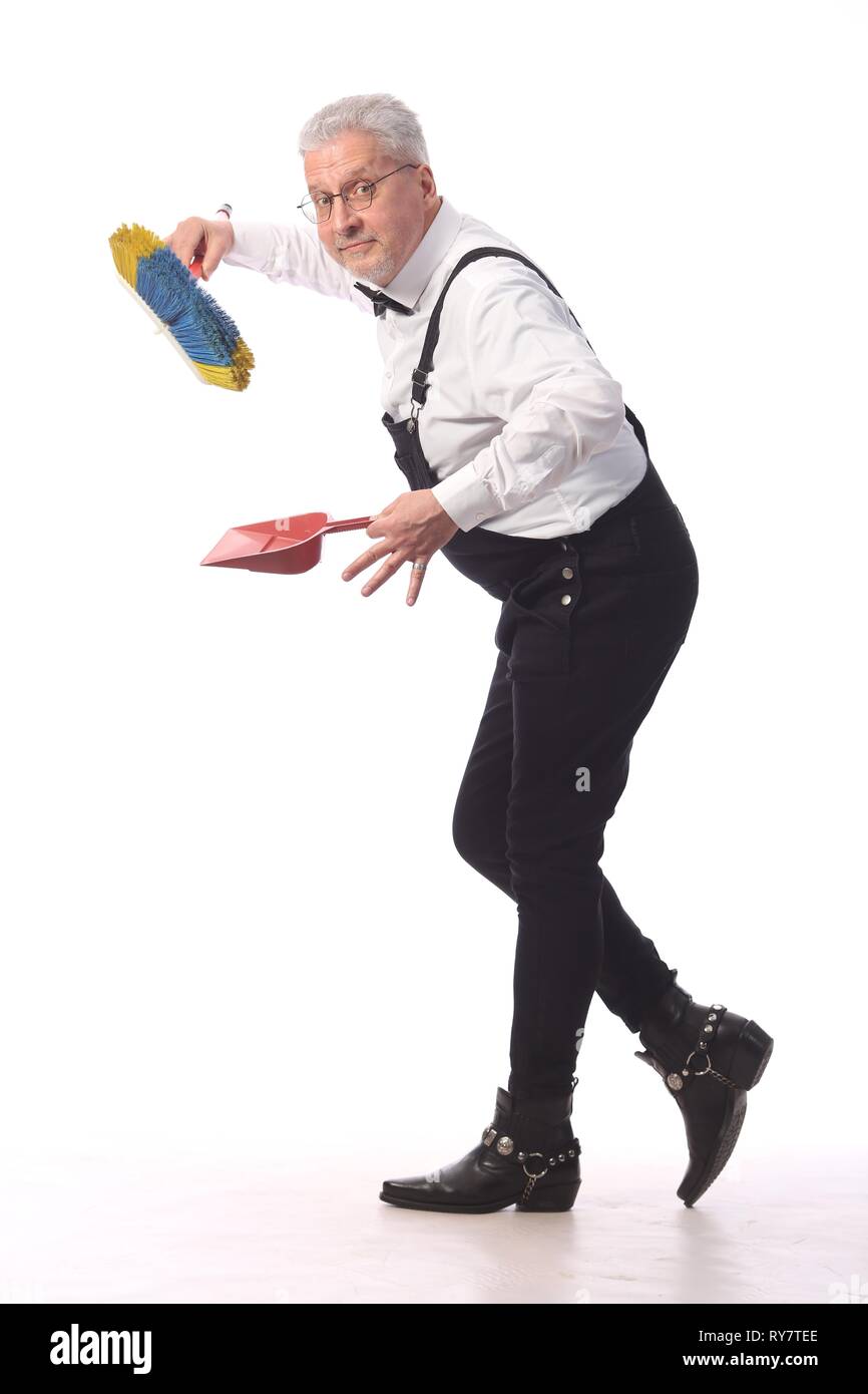 Grauhaarige Reiniger, Hausmeister in einem schwarzen Overall mit einem Mopp und Schaufel bietet Reinigung, auf weißem Hintergrund Stockfoto