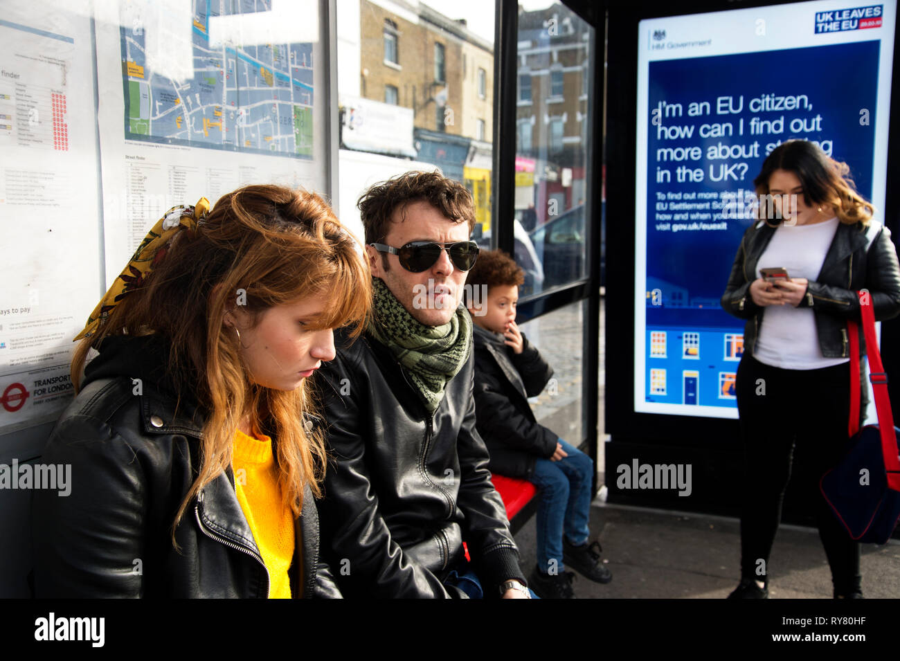 London. Hackney. Junges Paar in eine Bushaltestelle, die eine Regierung unterzeichnen erklären, was passieren wird, nach Brexit. Stockfoto