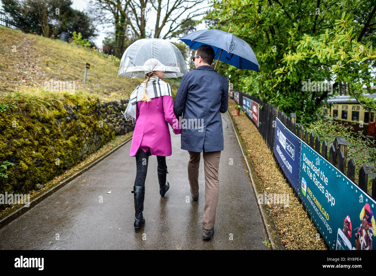 Menschen auf dem Weg zum Rennen in Cheltenham brolleys verwenden, da sie bei Cheltenham Racecourse auf der Gloucestershire Warwickshire Steam Railway von Toddington, wo ein besonderes Erbe Dampf Express Service ist die Rasse goers nach Cheltenham ankommen. Stockfoto