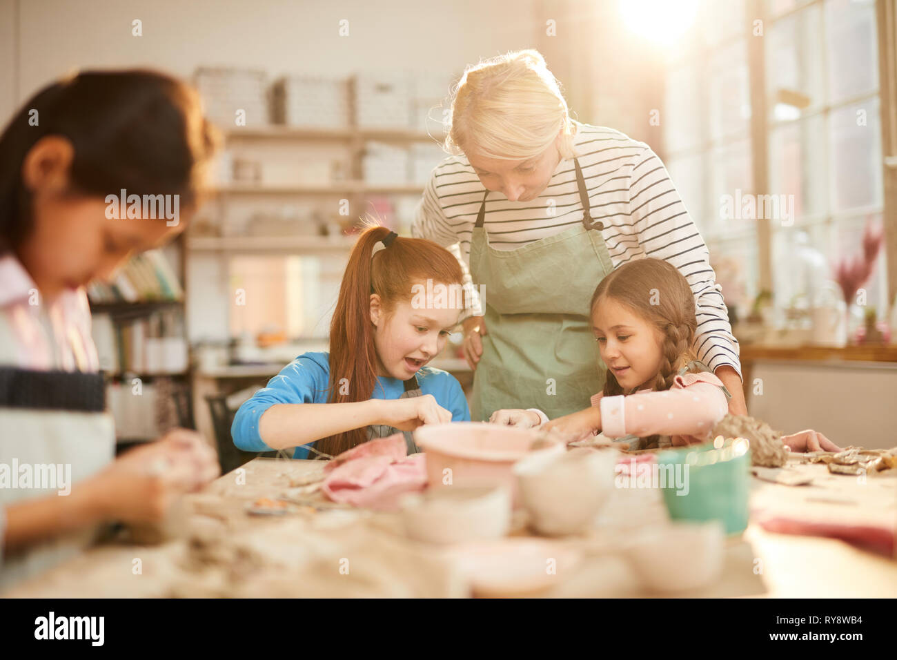 Portrait der weiblichen Kunst Lehrer, die mit Kindern arbeiten in der Keramik Klasse, Szene beleuchtet durch heitere Sonnenlicht, Kopie Raum Stockfoto