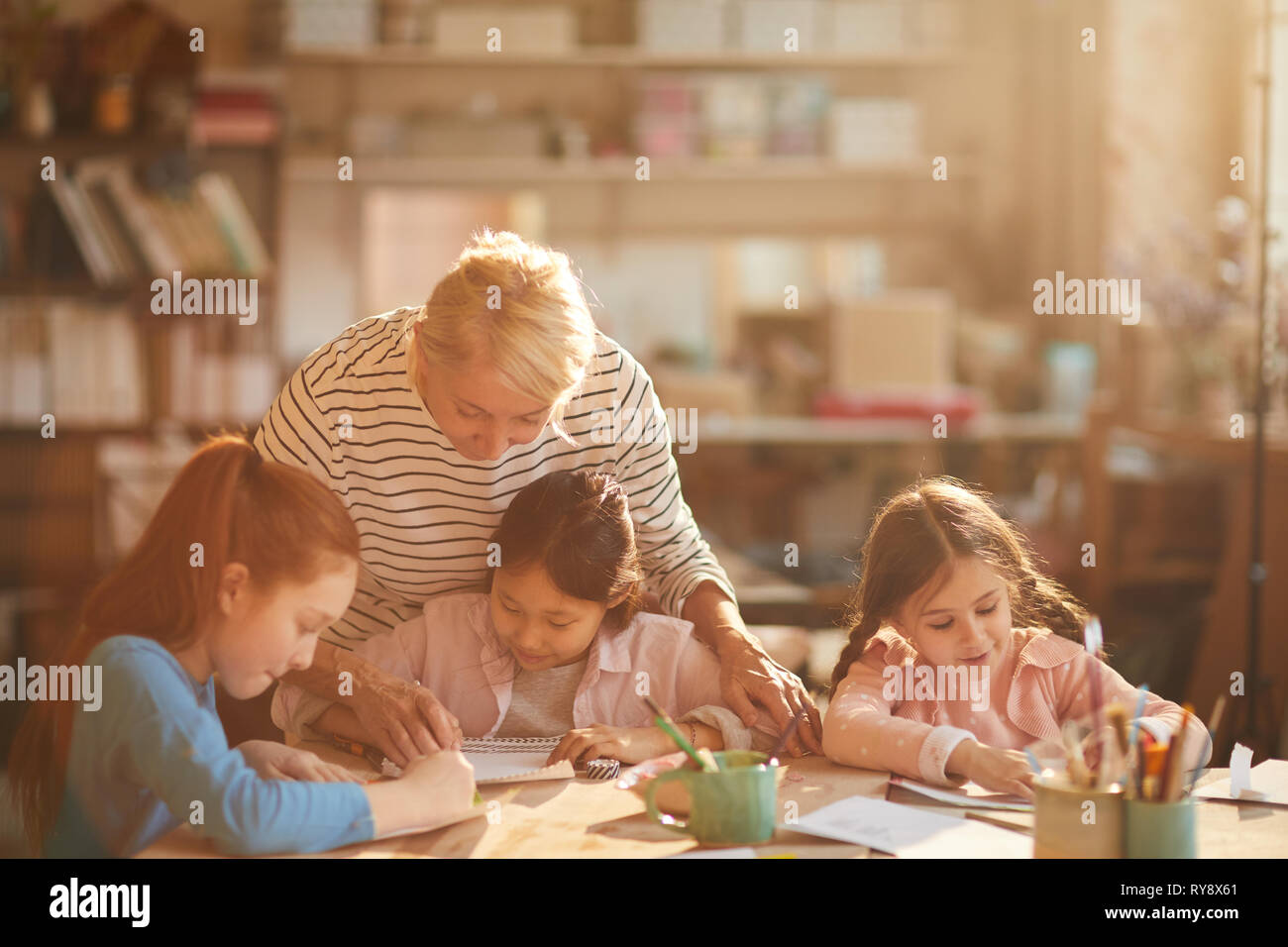 Portrait von reife Frau arbeitet mit einer Gruppe von kleinen Mädchen Malerei im Kunstunterricht, Szene beleuchtet durch heitere Sonnenlicht, Kopie Raum Stockfoto