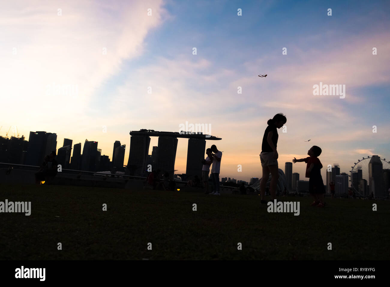 Mutter im Gespräch mit jungen Sohn im Marina Barrage, mit Singapur Skyline Sonnenuntergang Stockfoto