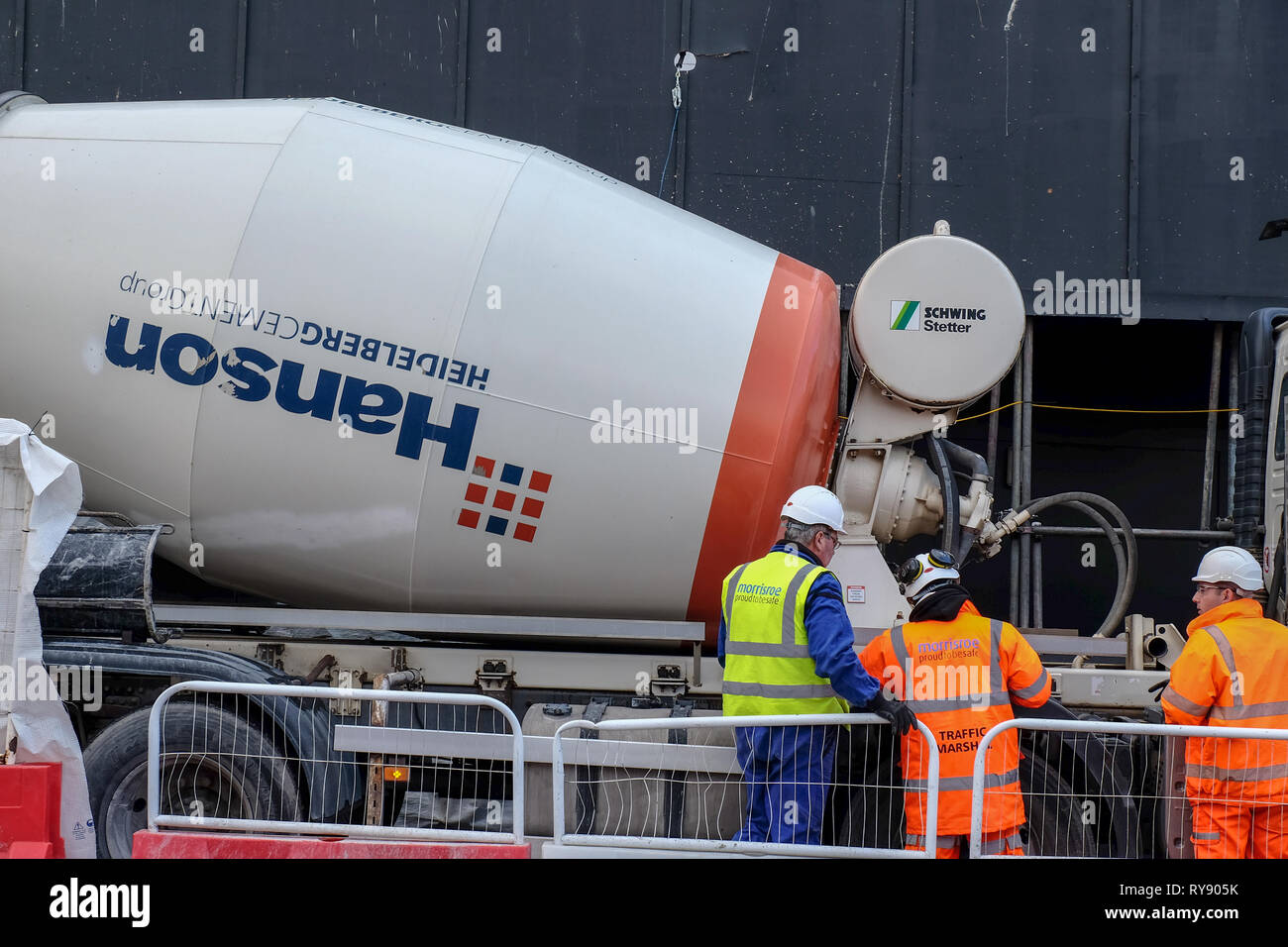 Die Bauarbeiter in Schutzhelmen und gelb und orange Jacken Blick auf einem betonmisch-Lkw markiert Hanson auf einer Baustelle in Central London, UK Stockfoto