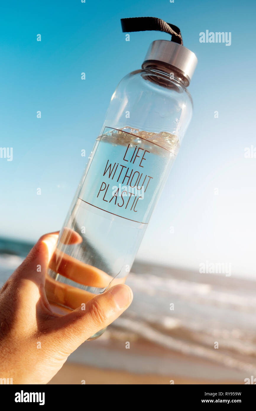 Nahaufnahme von einem kaukasischen Mann hält ein Glas wiederverwendbare Trinkflasche mit dem Text leben ohne Kunststoff in Es geschrieben, am Strand, mit dem Meer in der Stockfoto
