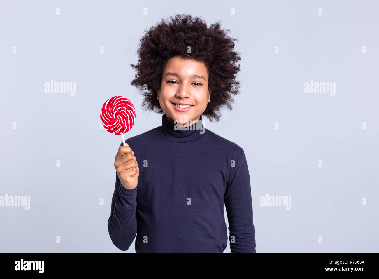 Lächelnd positive Dunkelhaarige Kind mit bunten Süßigkeiten auf Holzstab Stockfoto