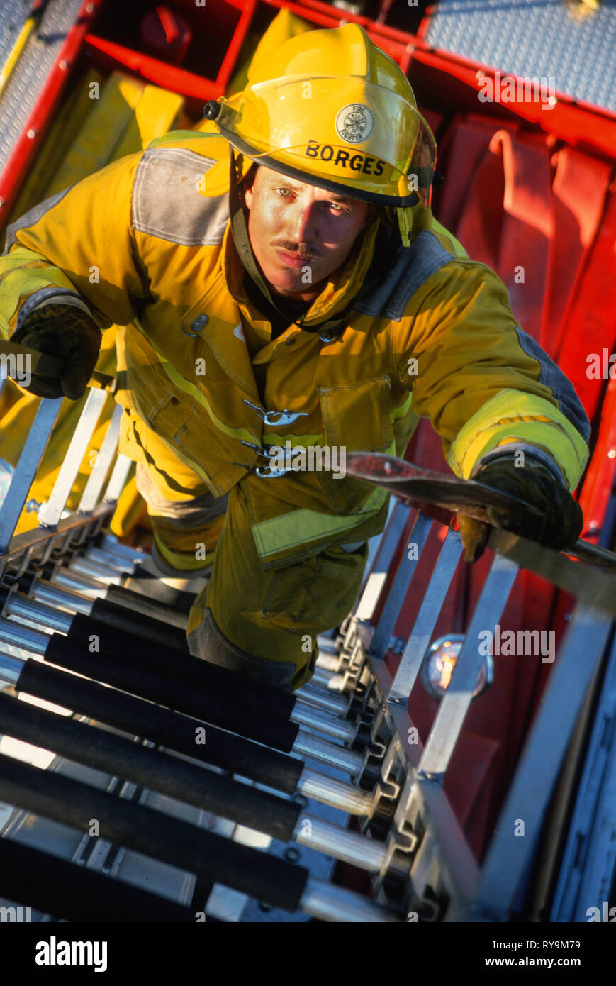 Der Feuerwehrmann klettert mit seiner Axt auf eine LKW-Leiter, USA 1997 Stockfoto