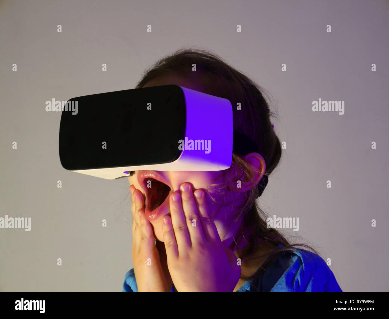 Junge Mädchen erleben VR-Headset Spiel auf farbigen Hintergrund. Kind mit einem Gaming Gadget für virtuelle Realität. Futuristische Brillen in jungen Jahren. Virt Stockfoto