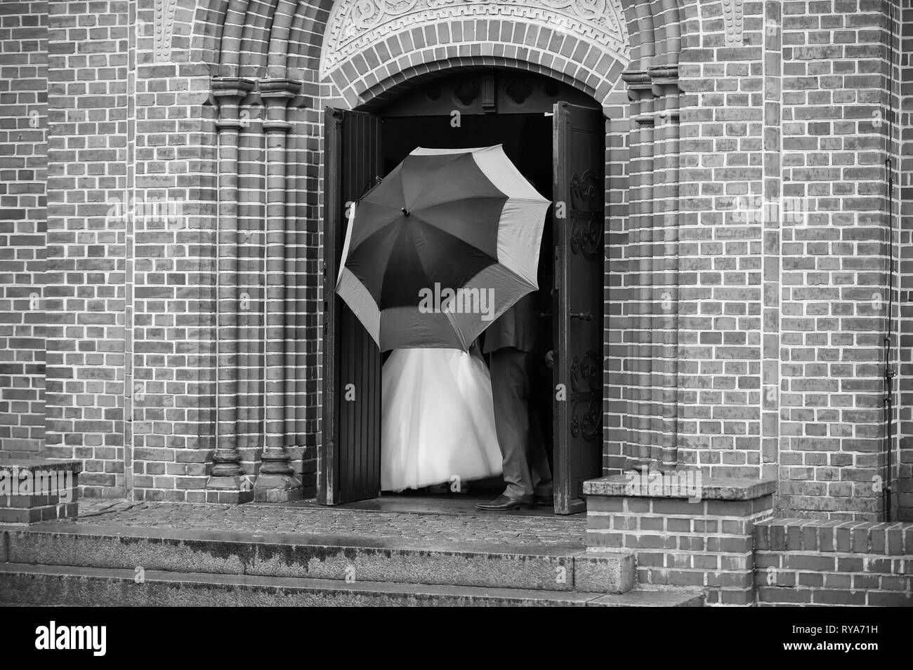 Ehepaar von Braut und Bräutigam hinter Sonnenschirm auf Kirche Tür auf Hochzeit Tag an regnerischen Wetter Stockfoto