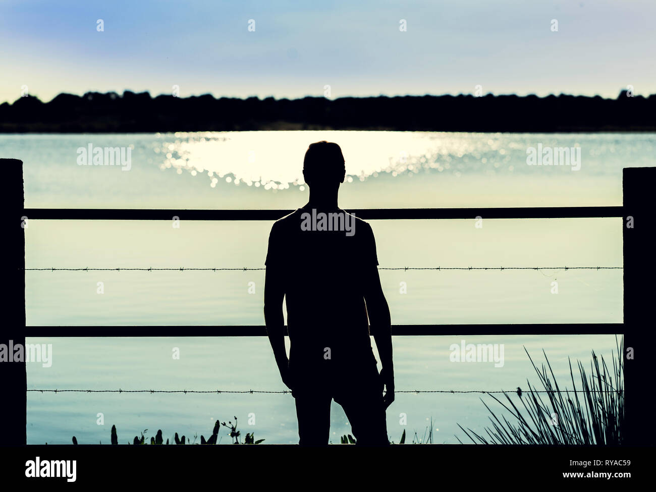 Silhouette Kerl in der Stacheldrahtzaun suchen das Wasser des Sumpfes in entspannter Körperhaltung Stockfoto