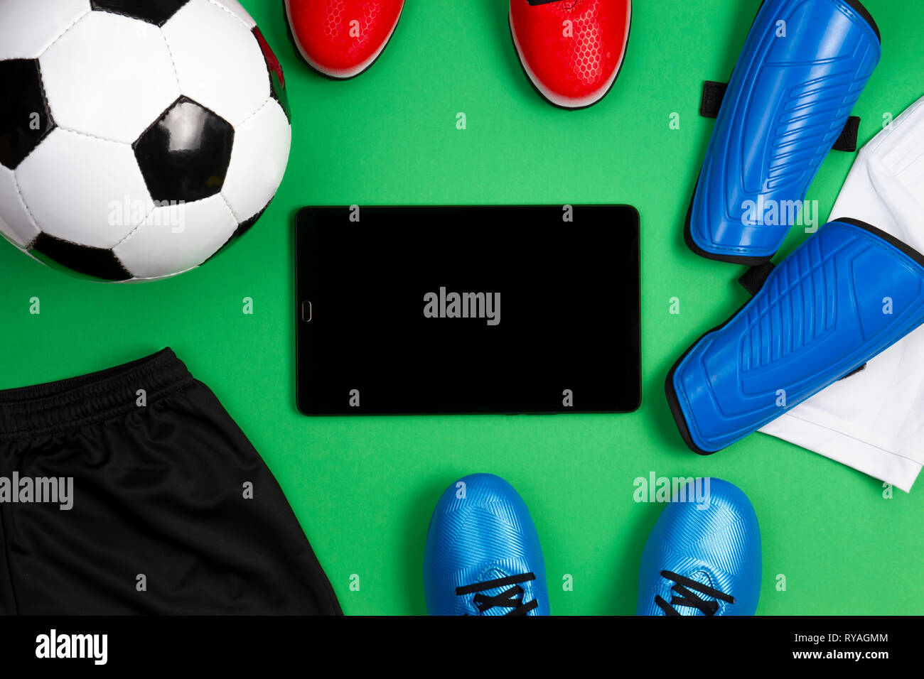 Fußball-Fußball-Hintergrund. Tablet Computer mit Fußball, blau Stiefel, Klampen, weißes T-Shirt und schwarze Shorts auf grünem Hintergrund. Ansicht von oben Stockfoto