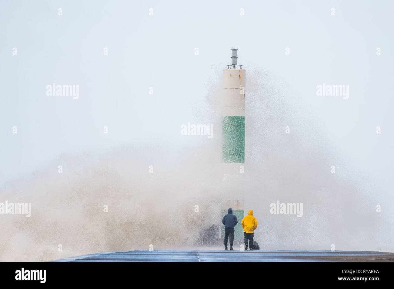 Aberystwyth, Großbritannien. 13 Mär, 2019. UK Wetter: Junge Männer Gefahren nehmen dramatische Fotos von sich selbst in der Nähe der Wellen als Gale force Winds aus Sturm Gareth - der dritte namens Sturm von 2019 - Aberystwyth auf der Cardigan Bay Küste treffen, West Wales UK am Mittwoch Nachmittag. Böen von bis zu 70 oder 80 mph sind in exponierten nördlichen Regionen Prognose, mit der Gefahr von schweren Sachschäden und erheblichen Betriebsunterbrechungen zu reisen und Power Services Photo Credit: Keith Morris/Alamy leben Nachrichten Stockfoto