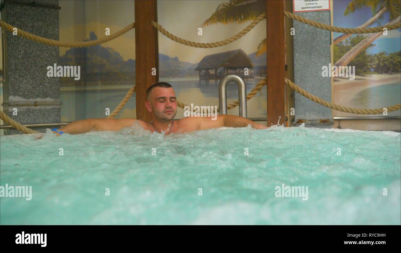 Jugendlich junge attraktive, stattlichen kaukasischen weißen brunette Kerl in Blasen Whirlpool, stehend im luxuriösen Spa Pool. Mann aus zurück, Freizeit, Entspannung, Massage Stockfoto